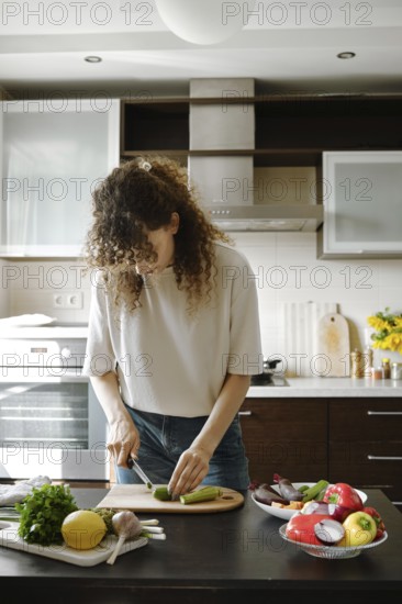 Young housewife chopping fresh baby zucchini on wooden board in the kitchen