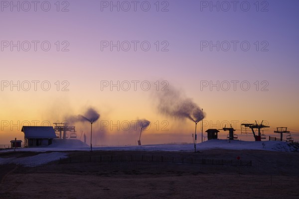 Snow cannons blow smoke under purple and orange evening sky, winter, Route de Cretes, Hohneck, La Bresse, Vosges, France