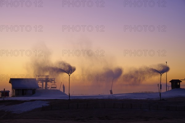 Under a dramatic sunset sky, snow cannons blow smoke across the empty hill, Winter, Route de Cretes, Hohneck, La Bresse, Vosges, France