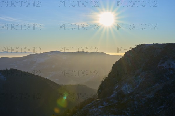 Sunrise behind mountains with bright sky and silhouette of a mountain ridge in a morning atmosphere, morning, winter, Hohneck, La Bresse, Vosges, France