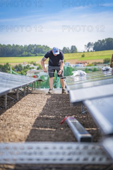 A technical worker installs solar panels on a construction site with a rural background, new Park and Ride Calw Heumaden car park on the new Hermann Hessebahn, Calw, Germany