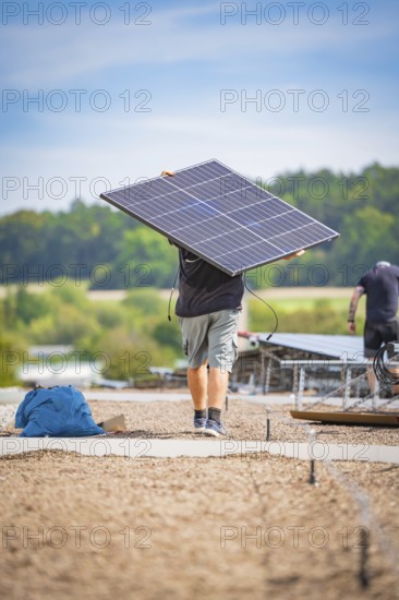 A man carries a solar panel on a construction site with a wooded background, new park and ride parking garage Calw Heumaden on the new Hermann Hessebahn, Calw, Germany
