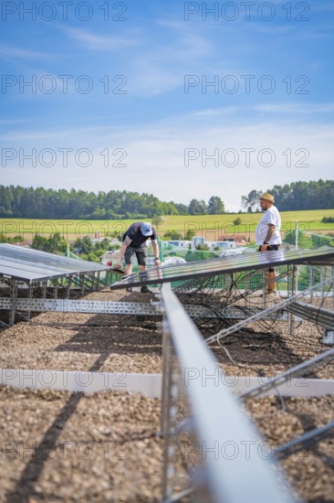 Two men install solar panels on a construction site surrounded by rural fields, new Park and Ride Calw Heumaden car park on the new Hermann Hessebahn, Calw, Germany