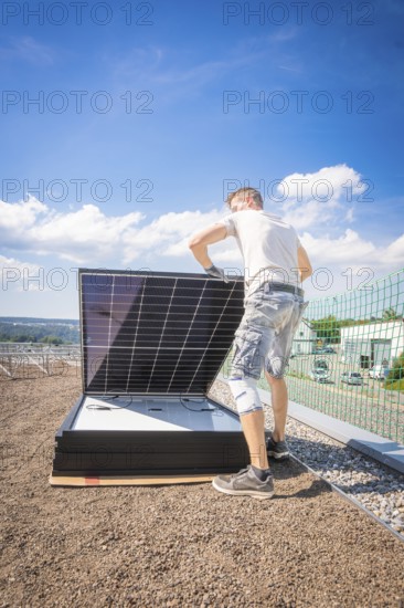 Person installs solar modules on a structure under a blue sky, new park and ride parking garage Calw Heumaden on the new Hermann Hessebahn, Calw, Germany