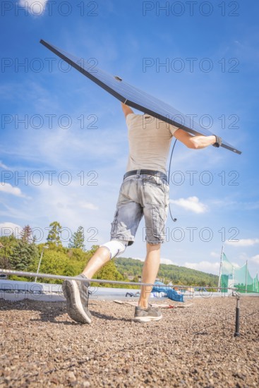 A worker lifts a solar module against the blue sky, new Park and Ride parking garage Calw Heumaden on the new Hermann Hessebahn, Calw, Germany
