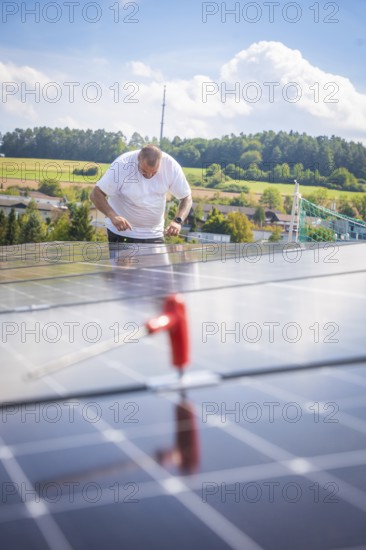 Worker checking solar modules in a landscaped area with clear skies, new park and ride Calw Heumaden car park on the new Hermann Hessebahn, Calw, Germany