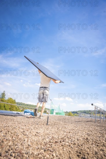 Person carrying a solar panel on a construction site with blue skies and nature, new park and ride parking garage Calw Heumaden on the new Hermann Hessebahn, Calw, Germany