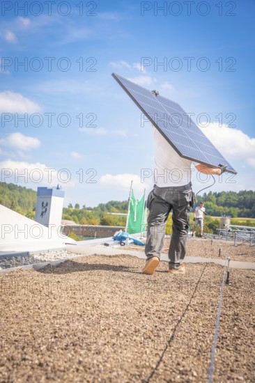 A worker carries a solar panel over the roof in sunny weather and blue skies, new park and ride parking garage Calw Heumaden on the new Hermann Hessebahn, Calw, Germany