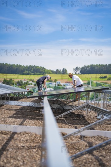 Two workers install a solar system surrounded by a quiet landscape under blue skies, new park and ride parking garage Calw Heumaden on the new Hermann Hessebahn, Calw, Germany
