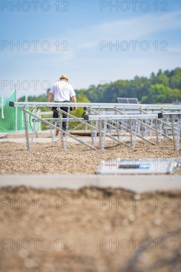 A worker assembles solar panel structures on a gravel roof under a blue sky, new park and ride parking garage Calw Heumaden on the new Hermann Hessebahn, Calw, Germany