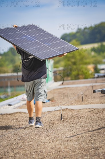 Man carrying solar panel on a gravel roof in front of a natural landscape, new park and ride parking garage Calw Heumaden on the new Hermann Hessebahn, Calw, Germany