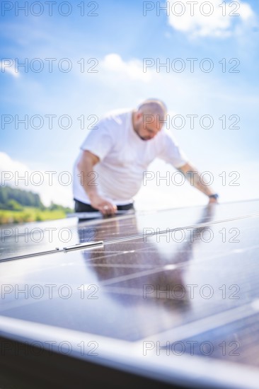 Man bends over a solar panel in a natural environment in bright light, new park and ride parking garage Calw Heumaden on the new Hermann Hessebahn, Calw, Germany