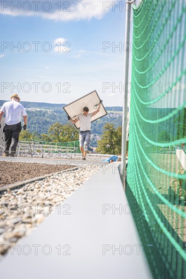 Worker carrying a solar panel on a construction site with a view of the mountains, new Park and Ride Calw Heumaden car park on the new Hermann Hessebahn, Calw, Germany