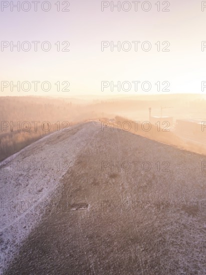 Hill covered by snow at sunrise with light fog, old deposit, construction site for PV open space plant, Lindenrain, Calw, Germany