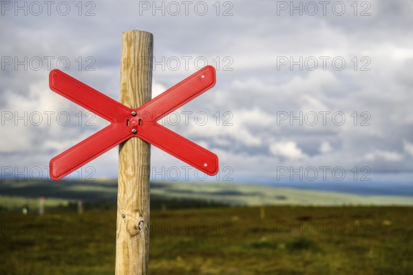 Red snowmobile snowscooter marker on a wooden post in front of a vast landscape under clouds, Kaunispää Caabuaivas, Lapland, Finland