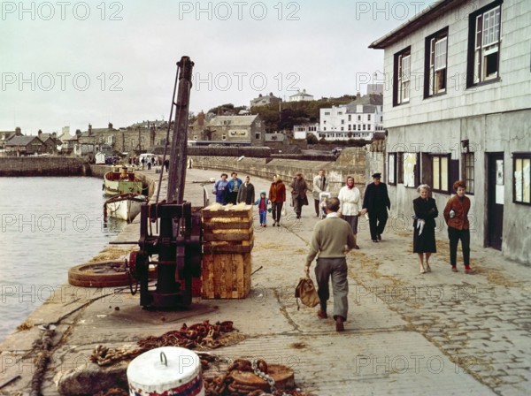 People walking along the quayside in the harbour at Hugh Town, Isles of Scilly, Cornwall, England, UK early 1960s