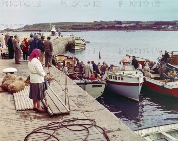 People boarding tour boats from the quayside in the harbour at Hugh Town, Isles of Scilly, Cornwall, England, UK early 1960s