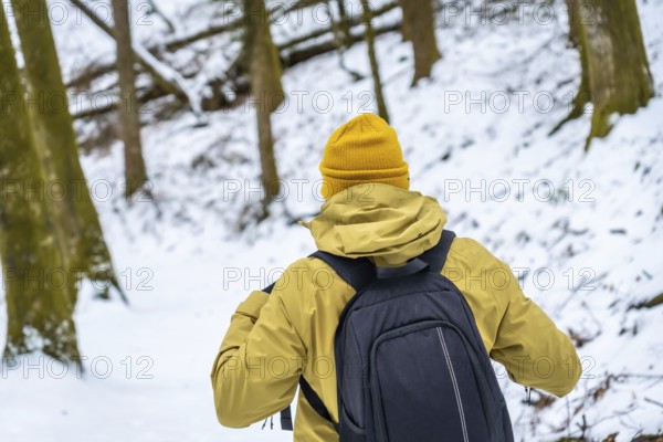 Hiker with backpack and yellow beanie navigating a snow covered forest, embracing the cold weather and the tranquility of winter exploration in nature