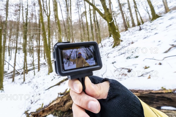 Hand holding an action camera showcasing a person recording a wide angle selfie video, creating content for vlogging or social media during a winter adventure in a snowy forest