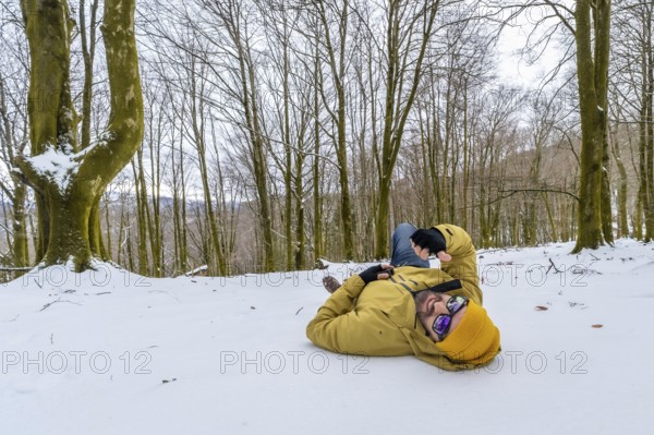 Man wearing a yellow winter jacket and hat, sunglasses, lying relaxed on the snow covered ground in a winter forest, enjoying a peaceful outdoor moment and cold weather