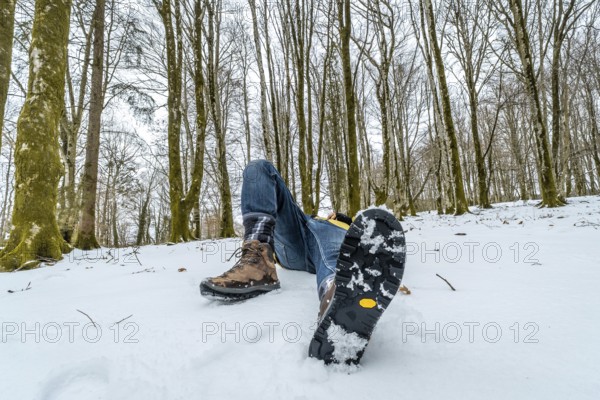 Person lying down in deep snow wearing warm hiking boots with a visible non slip sole, experiencing relaxation and freedom in the tranquil winter forest environment