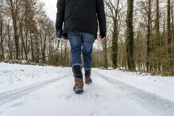 Person walking alone down a snow covered forest road in winter, wearing hiking boots and carrying a camera, capturing a tranquil moment of exploration and nature photography