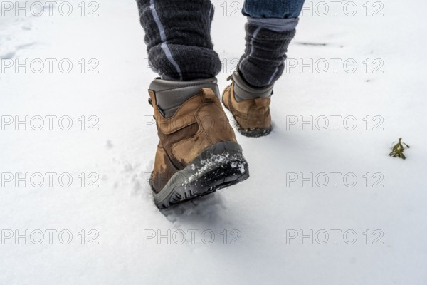 Person walking through fresh white snow in sturdy brown hiking boots and warm socks, leaving footprints on a tranquil winter trail during an active outdoor adventure
