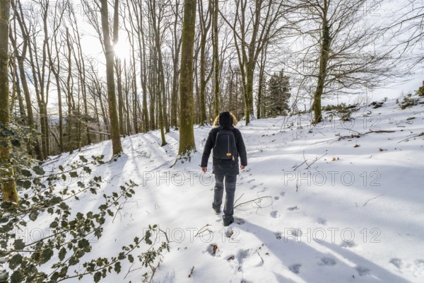 Person walking alone in a peaceful snow covered forest during winter, enjoying a serene outdoor trek and leaving footprints in the fresh powder under bright sunlight