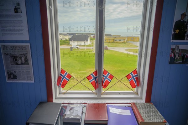 Window with Norwegian flags in the room, view of outdoor scene and books in the partisan museum in the old school of Kiberg on a wooden wall, Kiberg, Troms, Norway