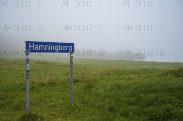 Town sign for Hamningberg on the Barents Sea in the midst of grassy landscape with fog and calm atmosphere, Hamningberg, Finnmark, Norway