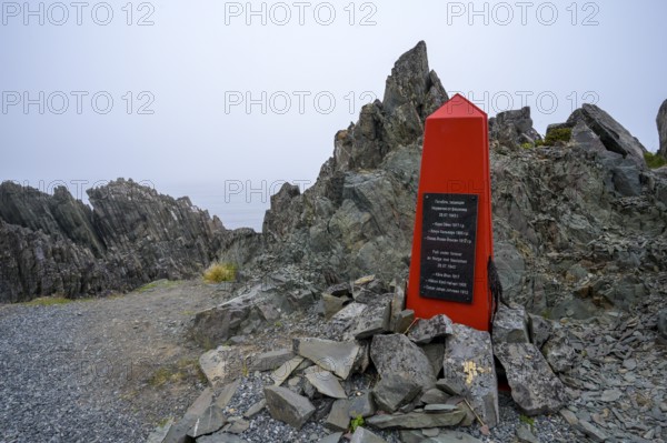 Red memorial to resistance fighters from the Second World War on rough rocks with fog in Norway, accompanied by a memorial plaque, Varanger Fjord, Barents Sea coast, Finnmark, Norway