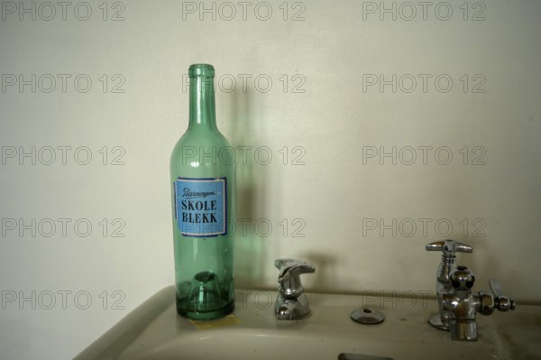 Green bottle with the Norwegian inscription Schukl ink a sink in front of a simple wall with retro atmosphere in the partisan museum in the old school of Kiberg on a wooden wall, Kiberg, Troms, Norway