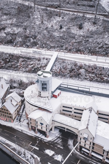 Modern building with snowy roof next to a snowy hill next to a river, Calw, Black Forest, Germany