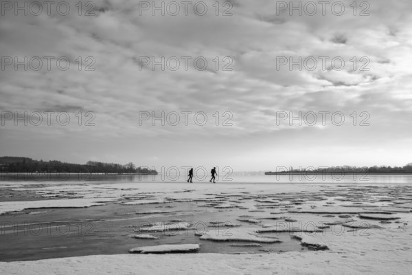 Two people walk across an icy water surface under a cloudy sky, black and white photography, Radolfzell am Lake Constance, Konstanz district, Baden-Württemberg, Germany
