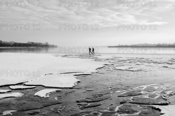 Two people walking on a frozen lake under a cloudy sky in a wintry landscape, black and white photography, Radolfzell am Lake Constance, district of Konstanz, Baden-Württemberg, Germany
