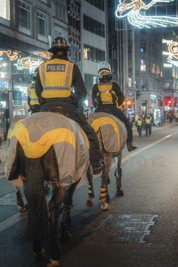 Police officers on horses patrol a brightly lit city street at night, London, England, Great Britain