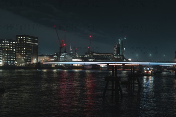River landscape with night lighting and visible cranes, London, England, Great Britain