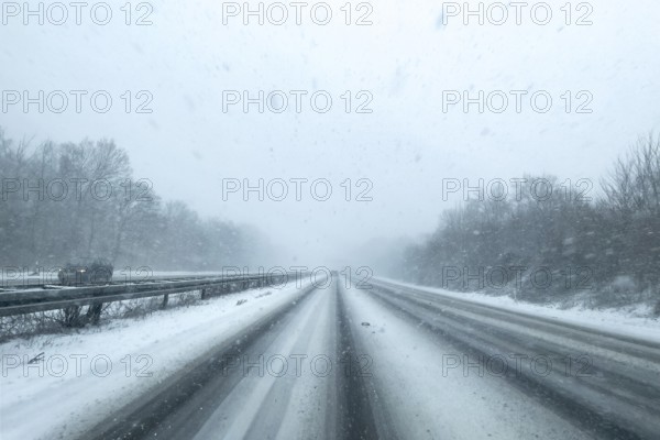 View through the windshield of a passenger car driving through light snowblowing on partly snow-covered motorway with lanes covered by snow, Germany