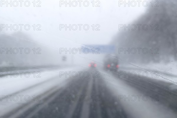 View through fogged windshield of cars driving through light snowblowing on partially covered freeway with lanes covered by snow, GermanyView through fogged windshield while driving through light snowblowing, Germany