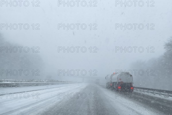 View through the windshield of a passenger car in poor visibility Driving through light snowblowing on partly covered freeway with lanes covered by snow, Germany