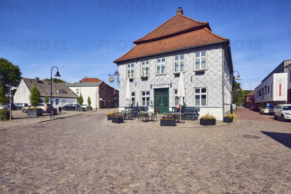 Alte Hofburg Imperial Palace pub, general architecture, commercial building, metal cladding, mansard roof, hipped roof, mansard hipped roof, red roof tiles, outdoor area of a restaurant with umbrellas, tables and benches, street made of paving stones, blue sky, cirrostratus clouds, Große Straße intersection with Rüschendorfer Straße, Damme, district of Vechta, Lower Saxony, Germany