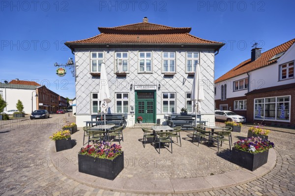 Alte Hofburg Imperial Palace pub, general architecture, commercial building, metal cladding, mansard roof, hipped roof, mansard hipped roof, red roof tiles, outdoor area of a restaurant with umbrellas, tables and benches, street made of paving stones, flower pots, blue sky, cirrostratus clouds, Große Straße intersection with Rüschendorfer Straße, Damme, district of Vechta, Lower Saxony, Germany