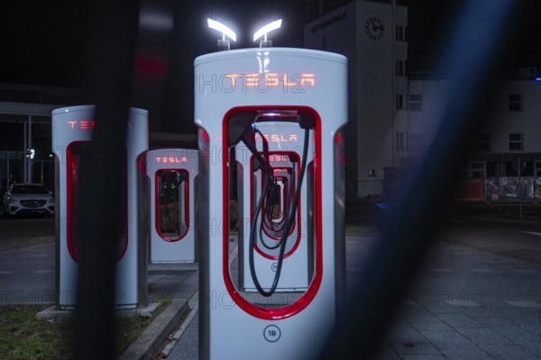 Several Tesla charging stations at night in bright red under city lights, Tesla Supercharger, Böblingen, Germany
