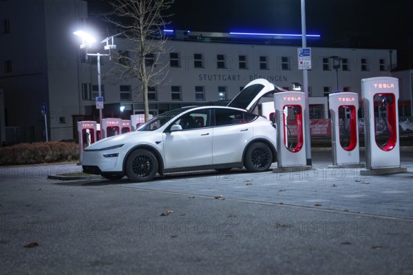 Parking lot with white Tesla at night, open rear, charging stations in the background, Tesla Supercharger, Böblingen, Germany