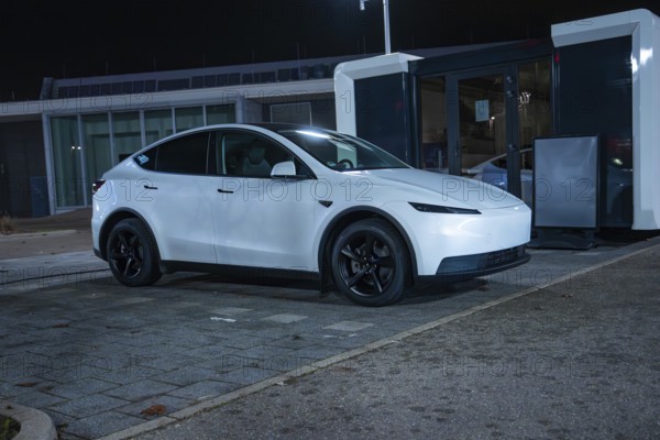 White Tesla parked at night at a charging station on grey asphalt, New Model Y Standard, Tesla Supercharger, Böblingen, Germany