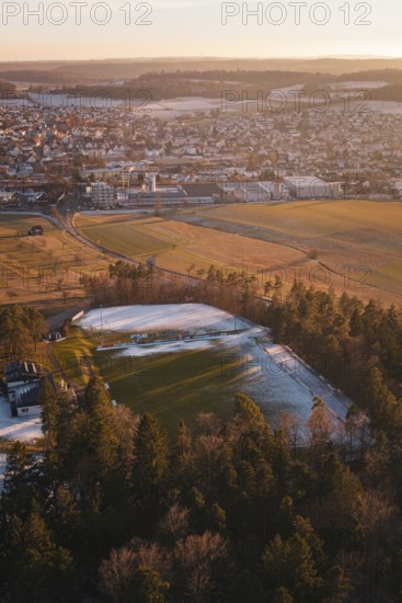 View of a snowy sports field near a town surrounded by trees and countryside, Althengstett, Calw district, Germany