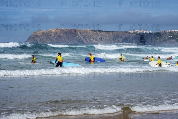 Participants in a surfing course go into the water, beach Praia de Vale Figueiras, village Arrifana in the back, western Algarve, Portugal