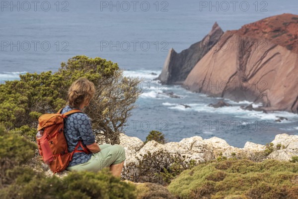 Hiking woman takes a break, view over cliff, Fishermens Trail, Rosa Vicentina, western Algarve just north of cape Cabo de Sao Vicente, Portugal