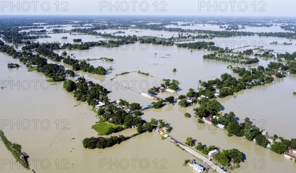 An aerial view shows widespread flooding submerging villages and farmland, with isolated homes and trees standing amid vast floodwaters