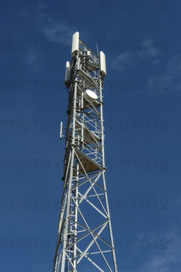 Tall silver telecommunications tower extends to a blue sky with wispy clouds on a sunny dayA tall telecommunications tower constructed of silver metal rises high against a clear blue sky with sparse, wispy white clouds on a bright, sunny day. France